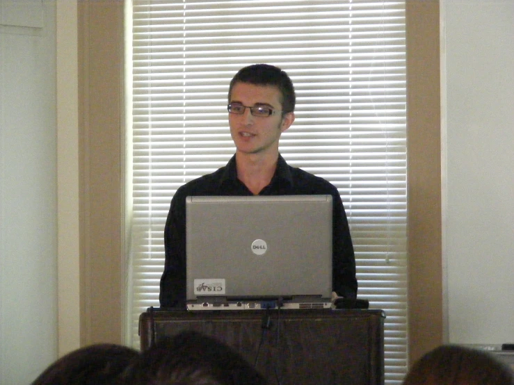 a man in black shirt standing in front of laptop