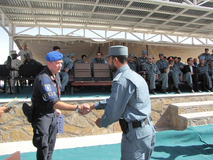 two policemen shake hands on a stage while spectators watch