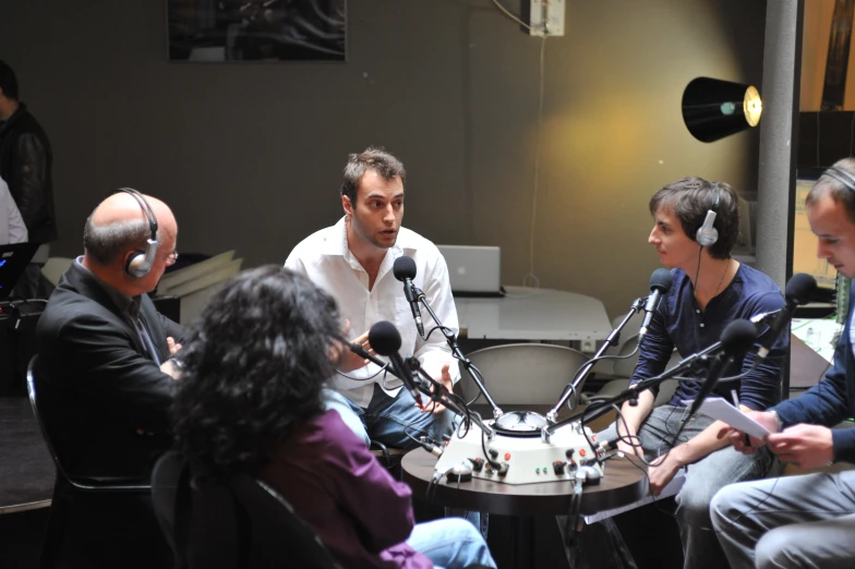 four people sitting and talking while surrounded by microphones