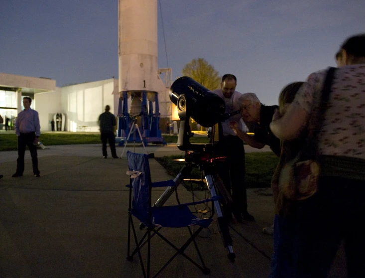 many people stand around a telescope at night