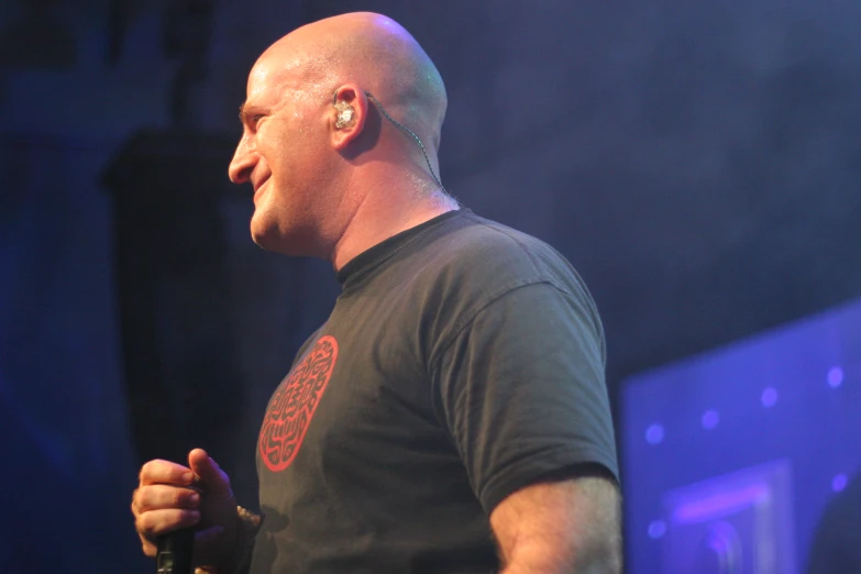 a man on stage in front of microphone with blue lighting