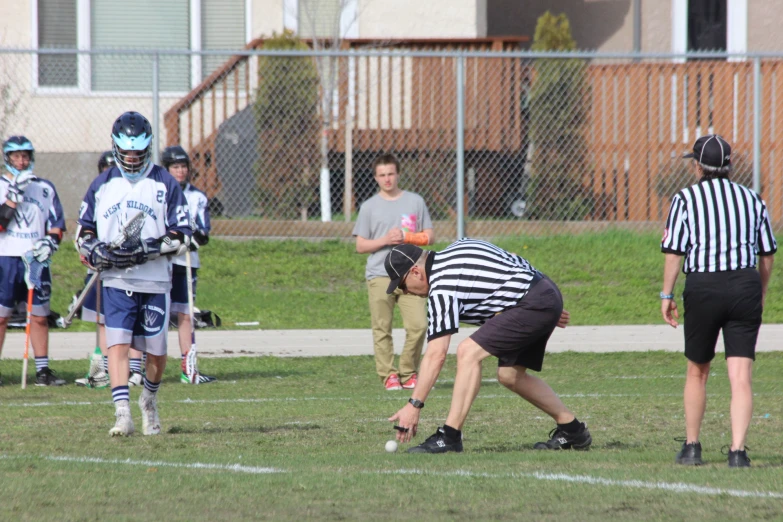 an umpire stands with his hand on the face of a goalie as a football player kneels down to block the ball