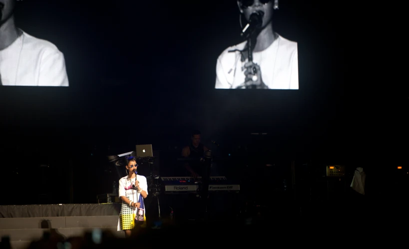 a man standing on stage, watching a projector screen with a couple of large black squares on it