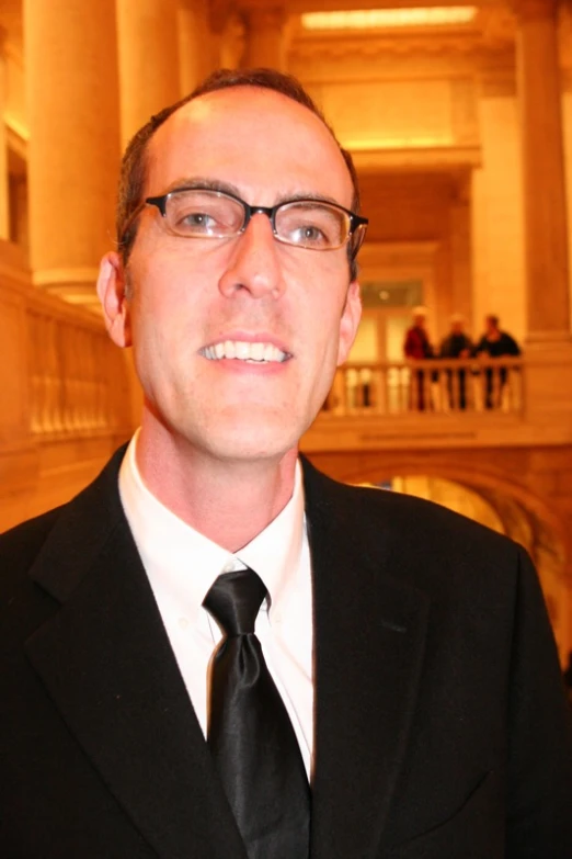 a man in black suit and tie in a room with stairs