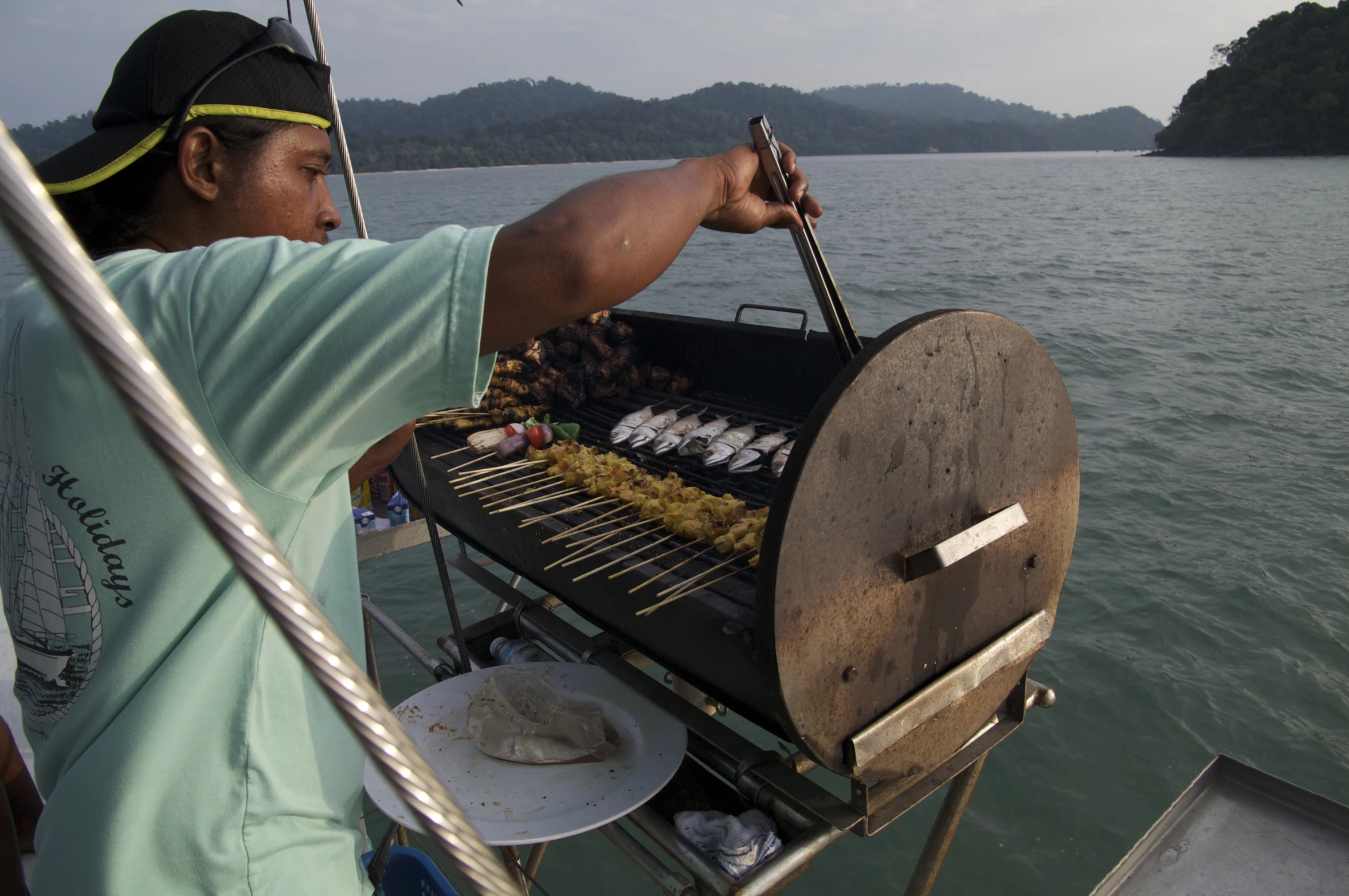 the man is cooking dinner on the grill by the water