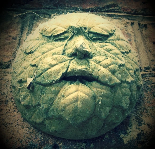 a sculpture of a green man face lying on the ground