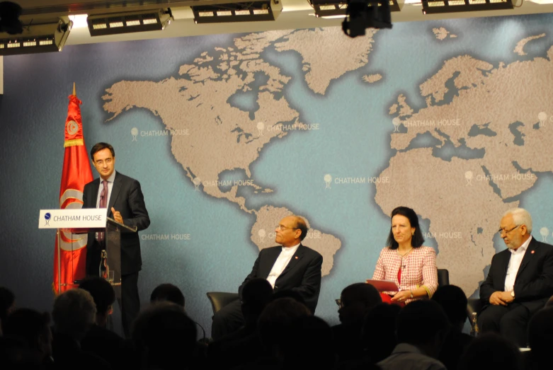 three people are at a panel, and a speaker is standing behind them