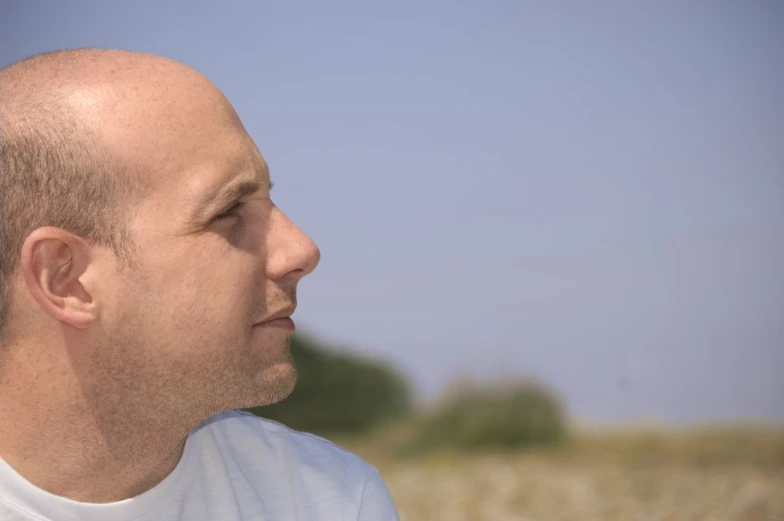 a bald man standing in a field looking straight ahead