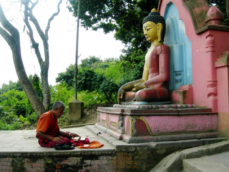 a person sitting next to a buddha statue in the middle of the day