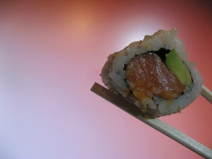 a roll with a cucumber and sauce on a wooden chopstick