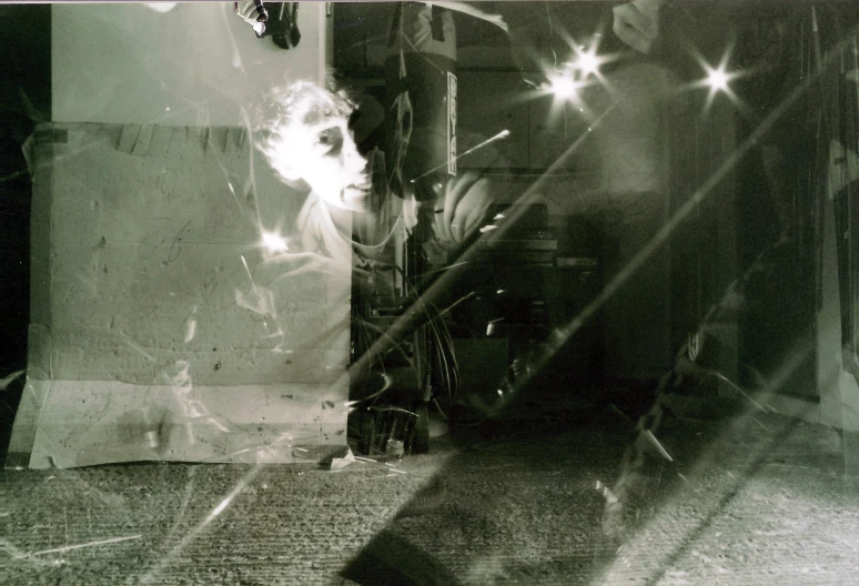 black and white pograph of a man standing in a dark room with his back to the camera as the sunlight comes out of the window and bright beams cast on the fabric