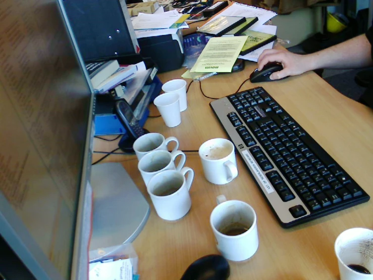 an office desk with many cups of coffee, a computer keyboard and various papers