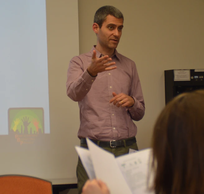 a man holding an open book standing in front of a class