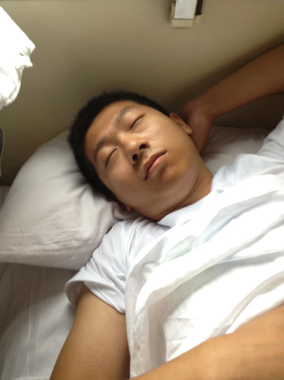 an asian man sleeping in bed on top of a pillow