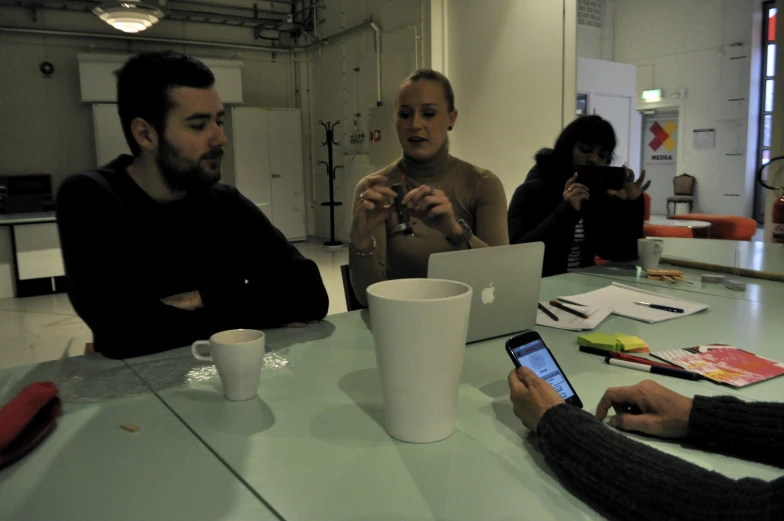 four people sitting at a table talking and looking at their cell phones