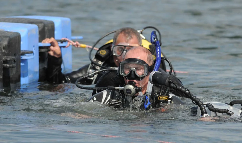 a man dives in water next to another guy in diving gear