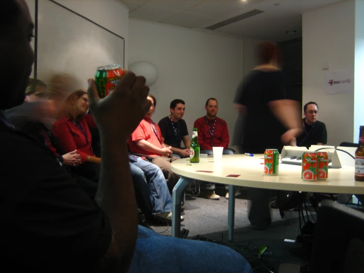 a group of men sitting around a table watching a person play nintendo wii