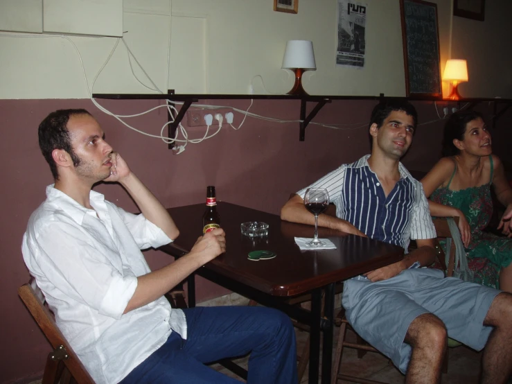 people sitting at small tables with bottles of beer in front of them