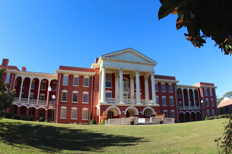 a large red brick building with a green grass field and trees