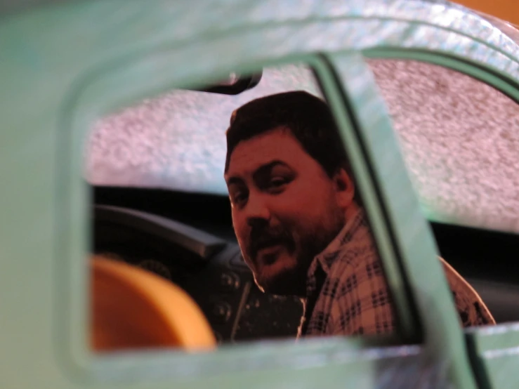 a man is reflected in a mirror of a green car