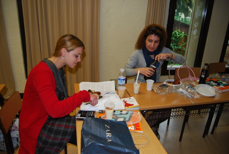 two women sit at a wooden table with an empty purse on it