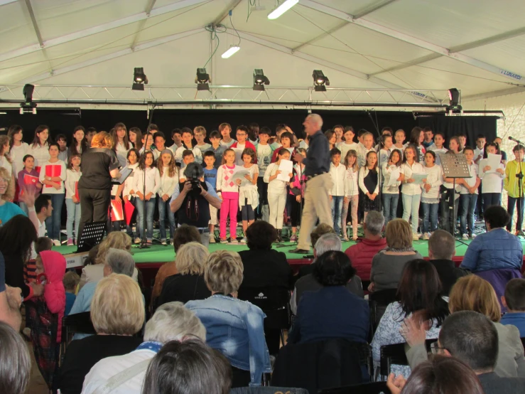 a crowd watches children sing on a stage