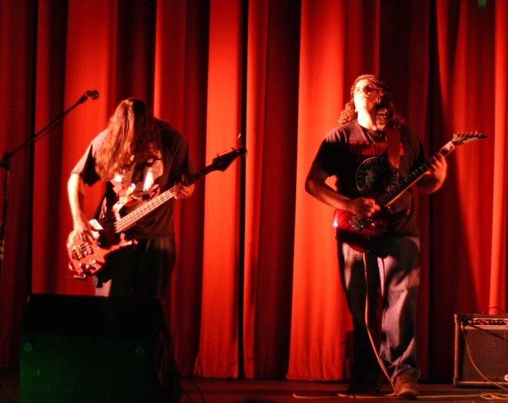 two male guitarists on stage in front of a red curtain