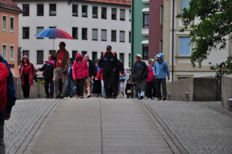 several people walking down a street, one holding a blue umbrella