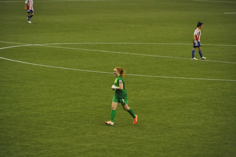 a woman in a green uniform on the field with her soccer ball