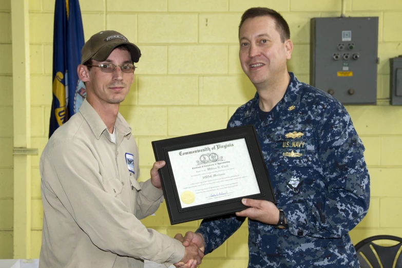 two service members are shaking hands as one is presented an award