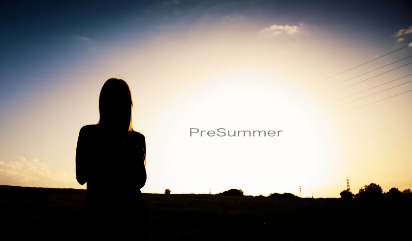 a woman stands in a field with the sun behind her