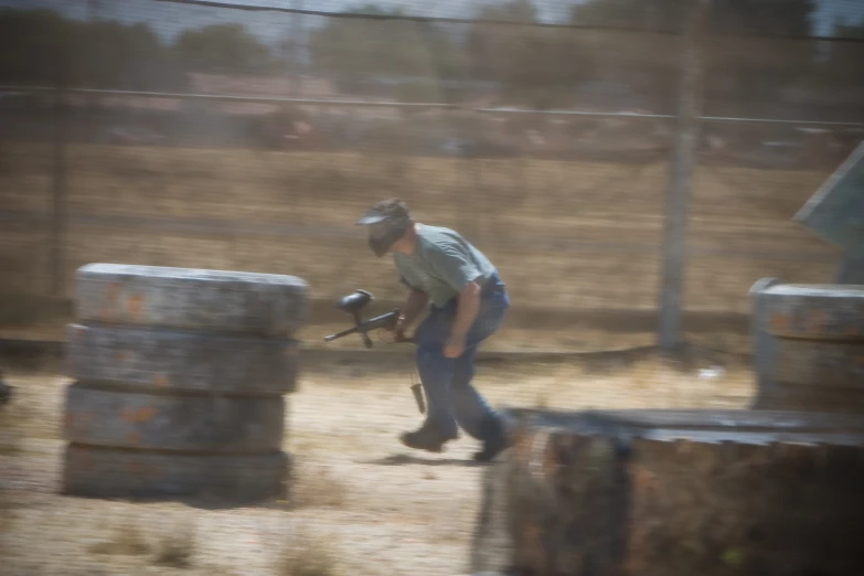 a man in grey shirt carrying a baseball bat near wooden barrels