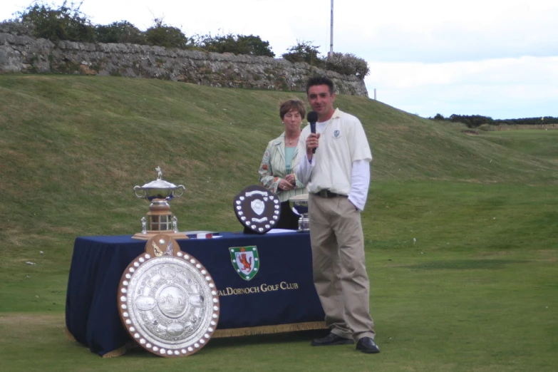 a man holding a microphone standing next to a table that has trophies on it