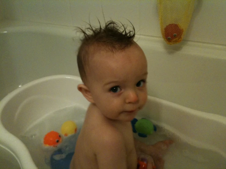 a baby sitting in the tub while playing with rubber ducks