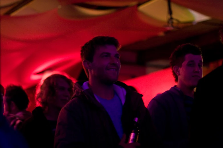 men are standing under a red tent and laughing