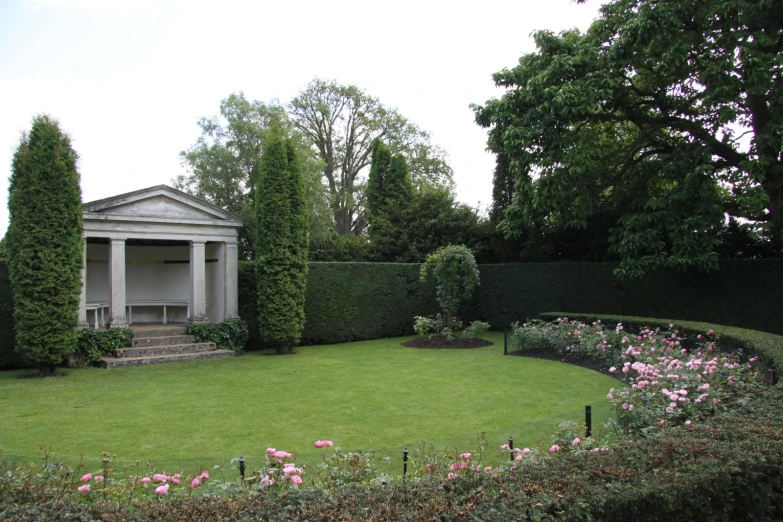 a grassy garden with rose bushes surrounding it and a house behind