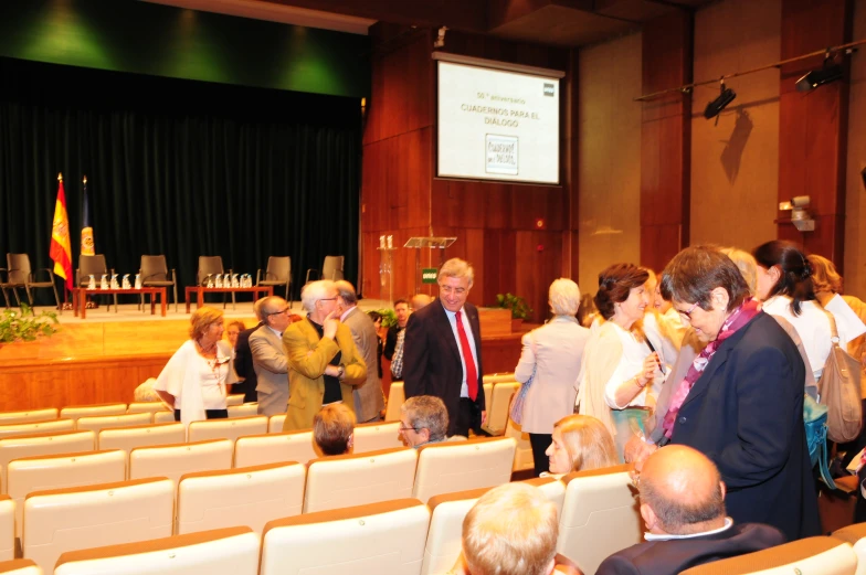 people talking at tables in large auditorium with flags