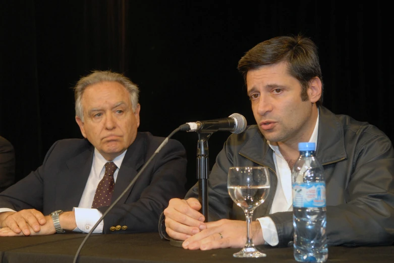 two men sit at a table with bottles of water