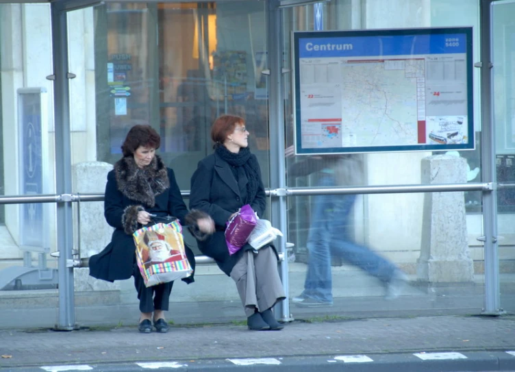 two people sitting on a bench next to a sign