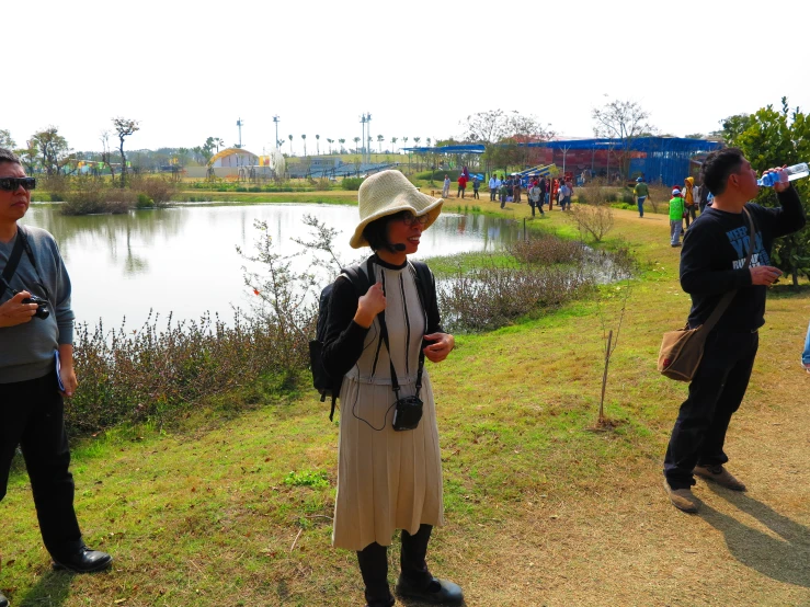 some people stand near a lake, one in a sun hat