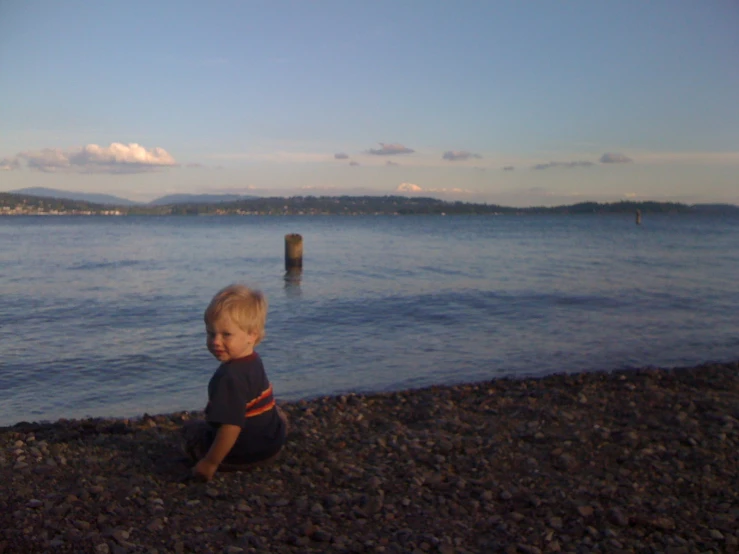 a young child sitting on the beach at twilight