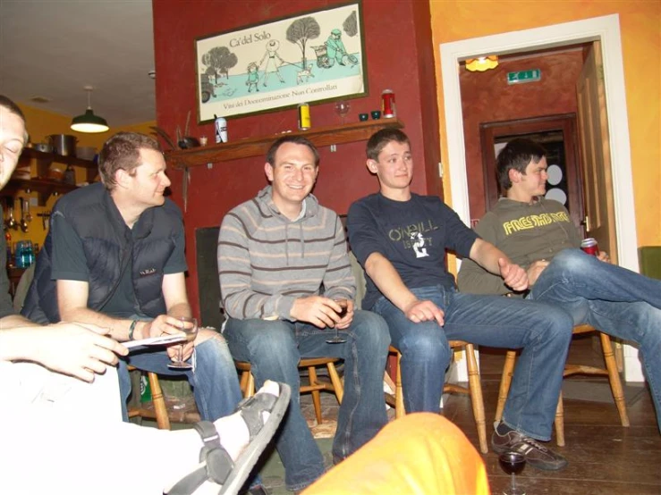 four men sitting in chairs in a room with a wine rack