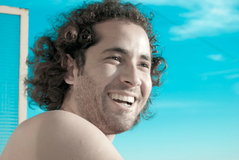 man with curly hair smiling against blue sky