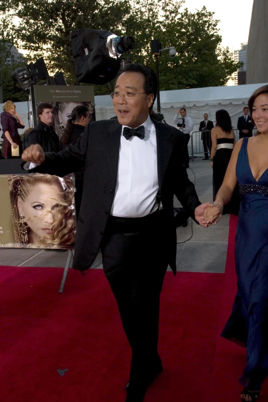 a man in a tuxedo and tie is leading a woman down the red carpet