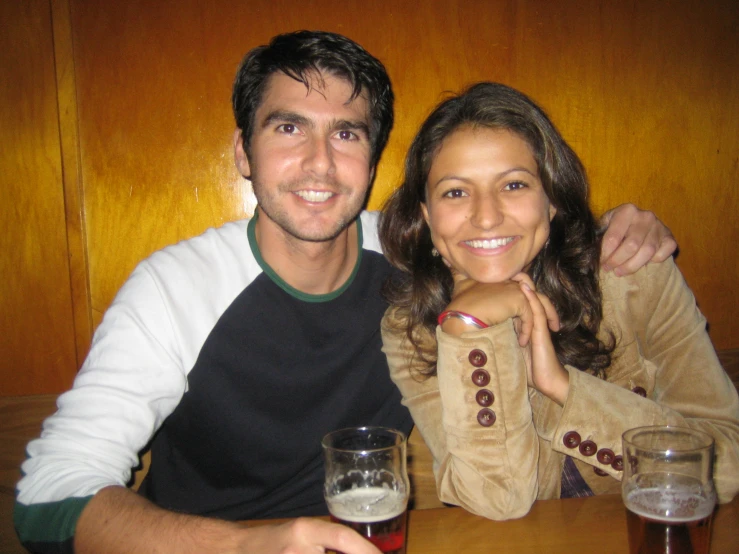 a couple sitting in a booth holding beer glasses