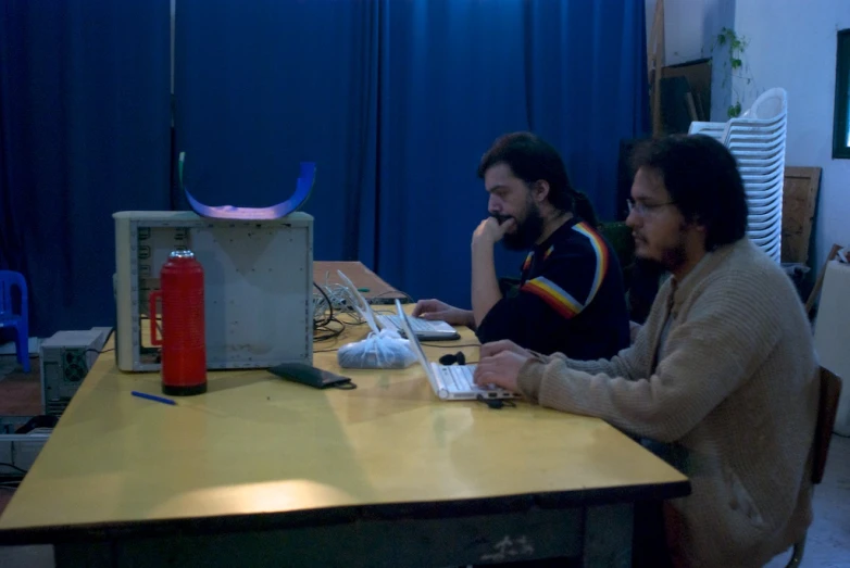 two people sitting at a desk in front of a laptop