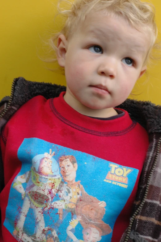 a small child has curly blonde hair and wears an old tee - shirt with toy story design on it