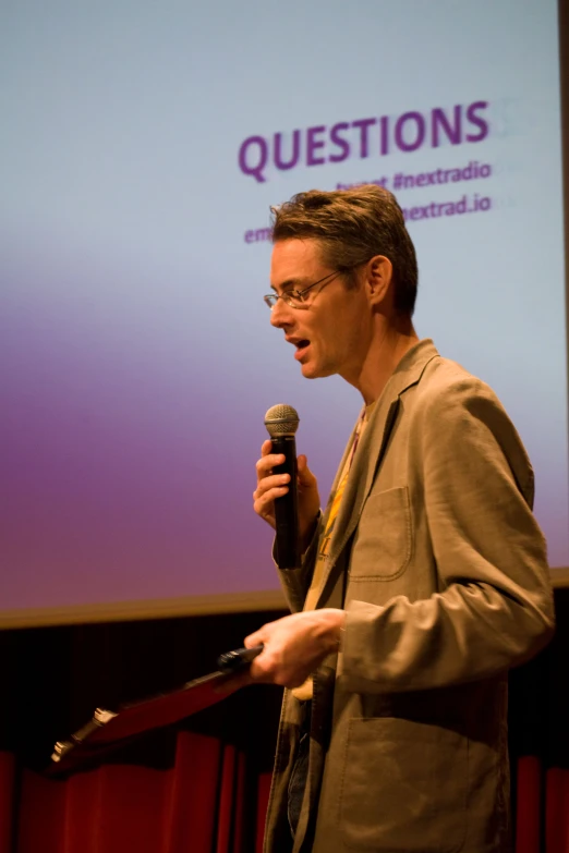 a man standing on a stage and holding a microphone in front of a banner