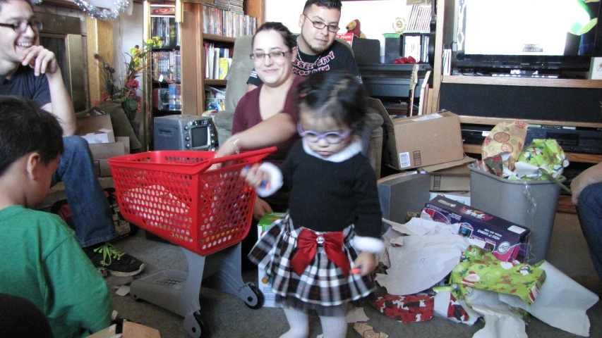 a small girl dressed up in a little dress and shoes stands in the living room as adults play video games