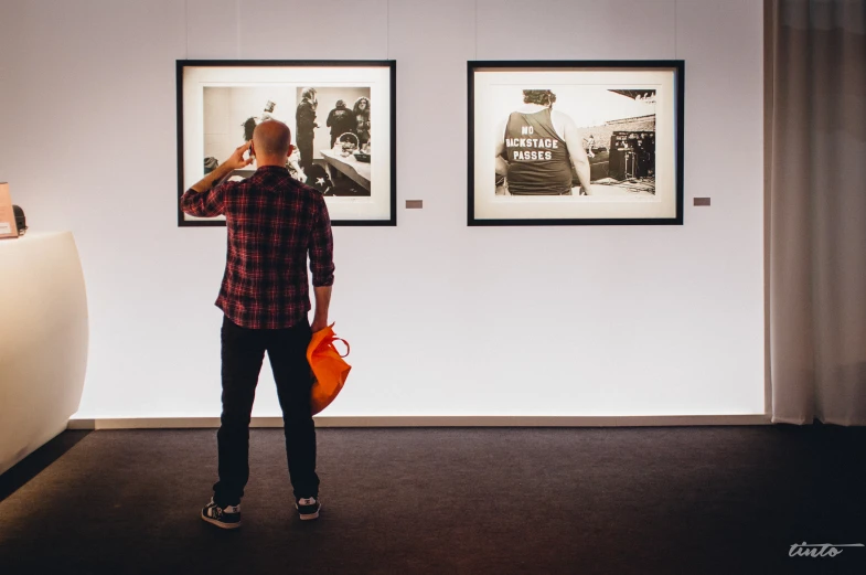 a man standing in an art gallery looking at paintings